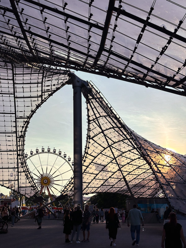 Stadtansicht des Zeltdachs im Münchner Olympiapark im Gegenlicht bei Sonnenuntergang mit Riesenrad, fotografiert von Max Sydow