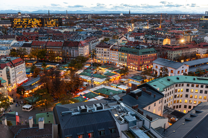Stadtansicht des Viktualienmarkts in München vom Alten Peter aus, mit Maibaum, Marktständen und Alpenpanorama bei Dämmerung, fotografiert von Max Sydow
