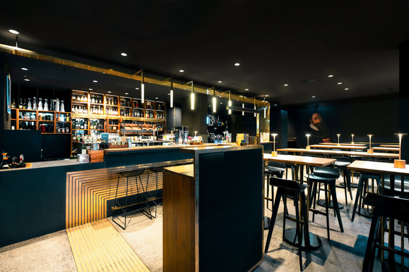Interior of the Herzog Bar Munich in evening atmosphere, dark elegant ambiance with an illuminated spirits wall, wooden bar counter and brass details, captured by Max Sydow