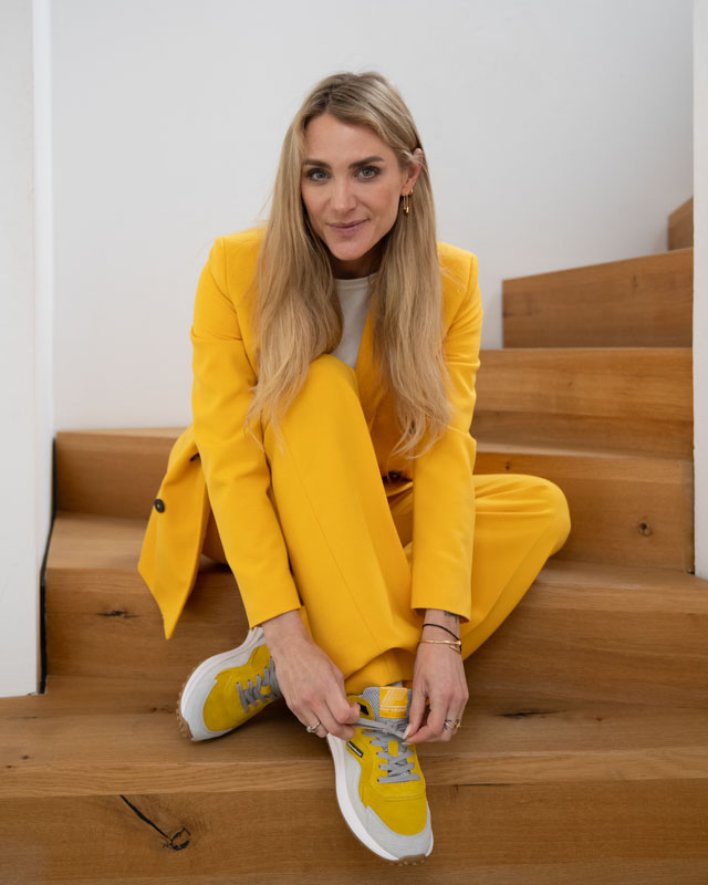 Editorial portrait of presenter Anna Kraft in a yellow suit sitting on a wooden staircase, captured by Max Sydow